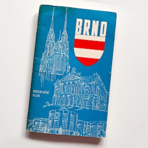 Pode incluir: Um guia de viagem vintage com uma capa azul com desenhos a traço branco de edifícios e a palavra "BRNO" em branco com um escudo vermelho e branco. O texto "ORIENTAČNÍ PLÁN" está impresso em branco.