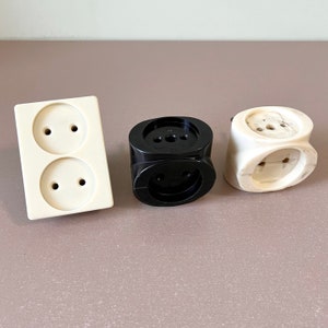 Puede incluir: Tres adaptadores de toma de corriente, uno blanco con dos tomas, uno negro con una toma y uno blanco con una toma. Todos son de plástico.