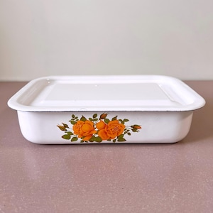 Puede incluir: Fuente de horno rectangular de esmalte blanco con tapa. La fuente presenta un diseño floral de rosas naranjas y hojas verdes. El borde tiene un ribete negro. Adecuado para hornear y servir.