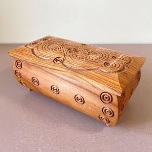 May include: A wooden box with intricate carvings of circles and geometric patterns. The box is light brown and has a slightly rounded shape.