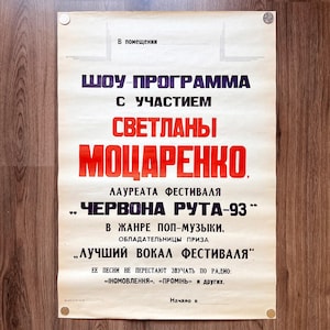 May include: A vintage poster in Cyrillic script, advertising a show featuring Svetlana Motsarenko. The poster has a cream background with red and blue text. It promotes the "Chervona Ruta-93" festival, mentioning pop music. The poster is displayed on a wooden surface.