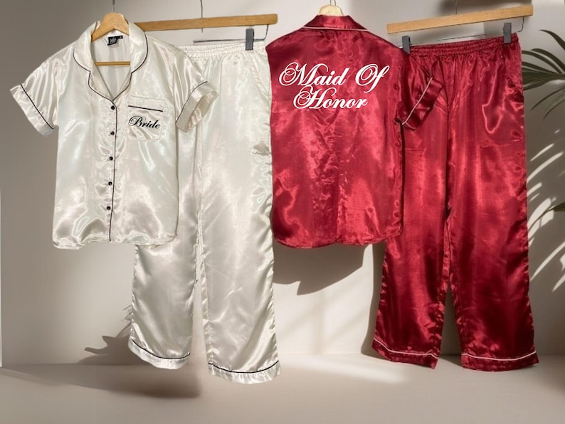 May include: Satin pajama sets in white and burgundy. The white set has "Bride" embroidered on the shirt. The burgundy set has "Maid of Honor" on the back. Both sets include a button-down shirt and pants.