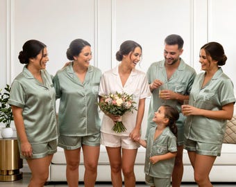 Puede incluir: Un grupo de personas con conjuntos de pijama a juego de satén verde salvia que consisten en camisas abotonadas y pantalones cortos, con una persona en el centro con un conjunto de pijama de satén blanco y un ramo de flores, todos con monogramas bordados.
