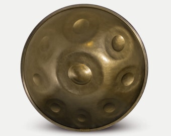 May include: A gold-colored handpan with a circular shape and multiple indentations. The handpan has a slightly raised rim and a smooth surface.