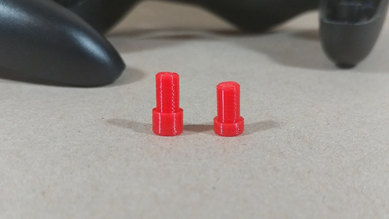 May include: Two red plastic joystick caps for a video game controller.