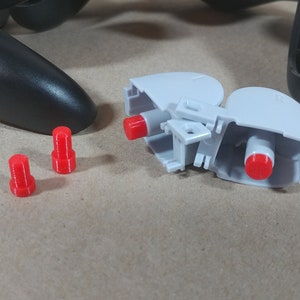 May include: A disassembled video game controller with three red plastic buttons and a gray plastic housing.