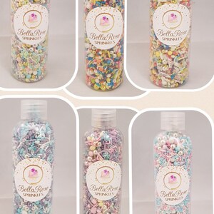 Puede incluir: Seis botellas de plástico transparentes llenas de espolvorear de colores. Cada botella tiene una etiqueta blanca con el texto "Bella Rose Sprinkles".