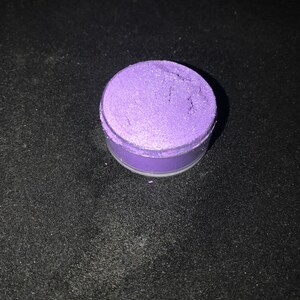 May include: A small round container filled with purple glitter. The glitter is a fine, iridescent purple color.