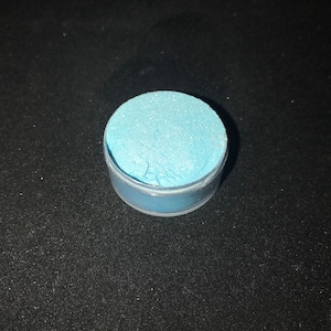 May include: A small round container filled with light blue glitter.