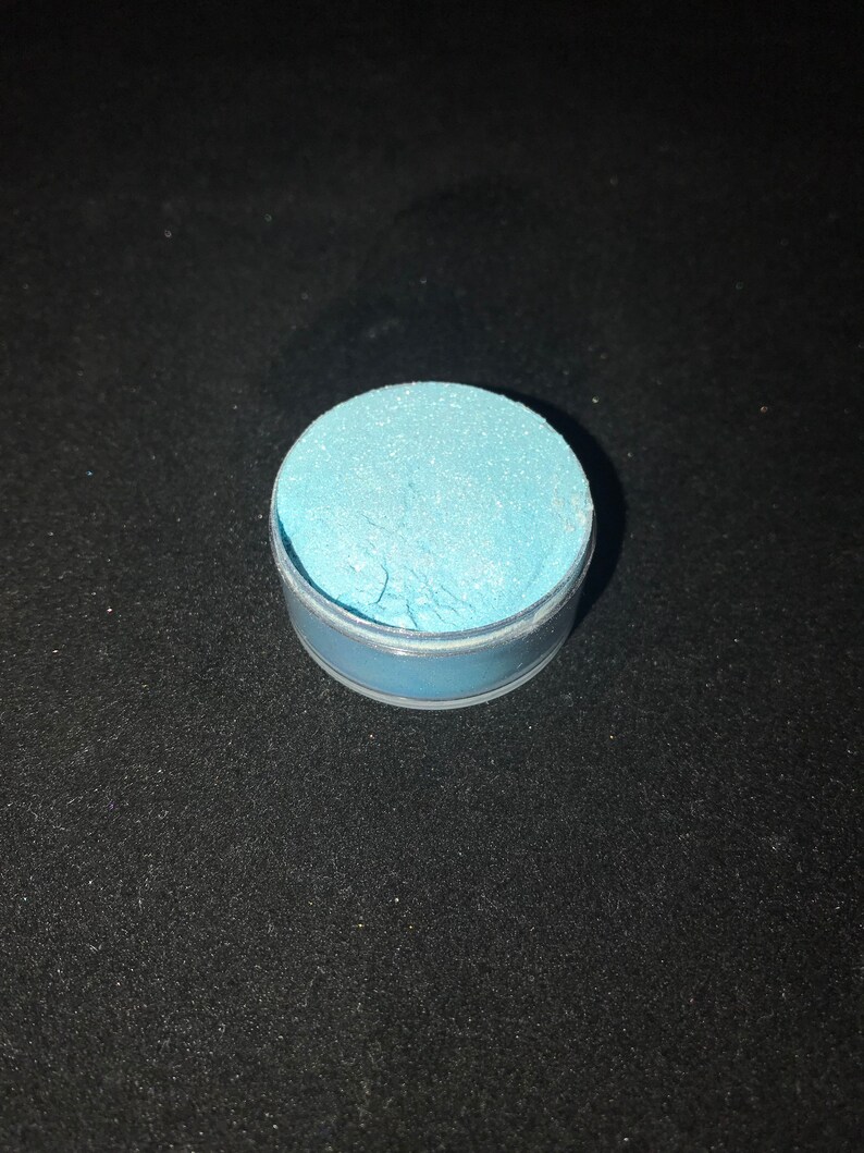 May include: A small round container filled with light blue glitter.