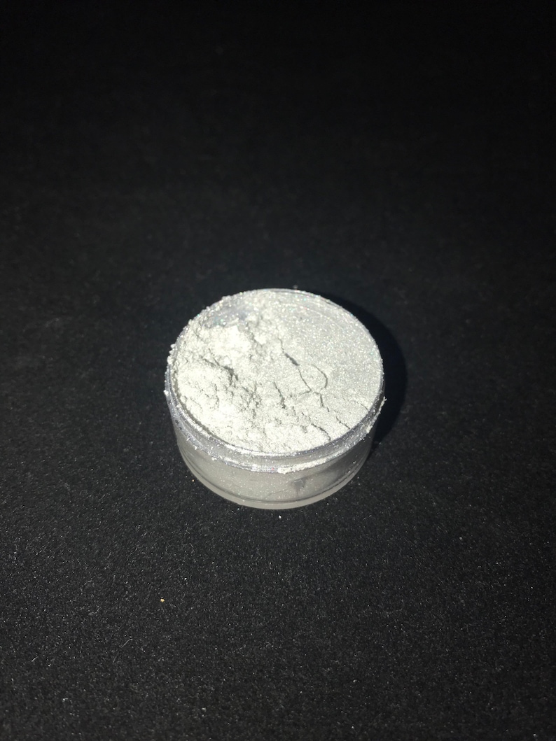 May include: A small, round container filled with a white, shimmery powder. The powder is likely used for crafting or cosmetic purposes.