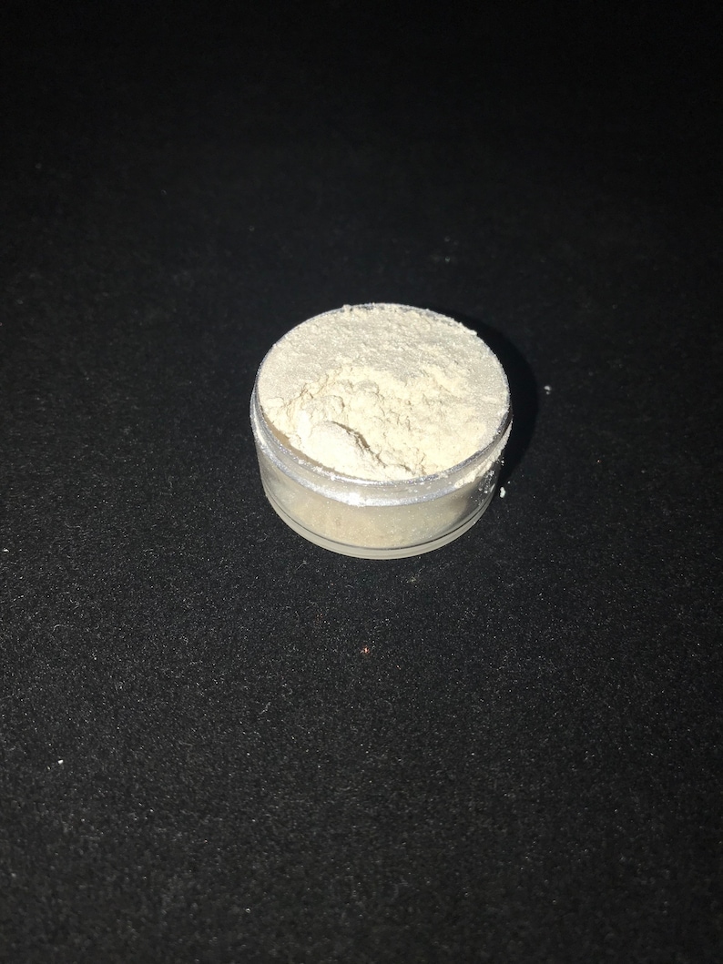 May include: A small, clear plastic container filled with a white powder. The container is sitting on a black surface.