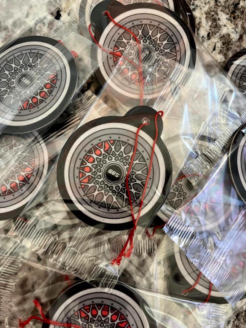 Puede incluir: Varios ambientadores para coche con un dise&ntilde;o de rueda con detalles grises, negros y rojos. Cada ambientador redondo tiene una cuerda roja para colgar. El dise&ntilde;o incluye el texto "BBS".