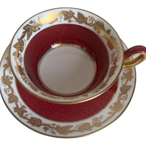 Peut inclure: Une tasse à thé et une soucoupe en rouge et or avec un motif de vigne. La tasse et la soucoupe sont toutes deux décorées d'une bordure dorée et d'un motif de vigne.