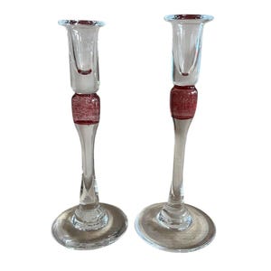 May include: A pair of clear glass candle holders with a red and white swirl design around the base.