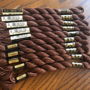 May include: A collection of brown DMC embroidery floss skeins. Each skein is labeled with a number and brand information. The floss is tightly wound and appears to be made of a soft, durable material. The image shows several skeins of the same color.