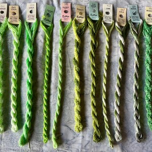 May include: Ten skeins of EdMar rayon embroidery thread in various shades of green, ranging from light lime to deep olive. Each skein is attached to a paper tag displaying the brand name, color number, style name, and length in yards or meters.