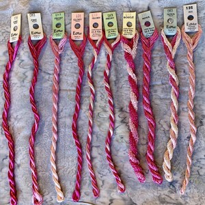 May include: Nine skeins of EdMar rayon embroidery thread in various shades of pink, red, and peach. Each skein is attached to a paper tag labeled with brand name, color name, number, and length in yards, including 10.5, 16, 20, and 21.5 yards.