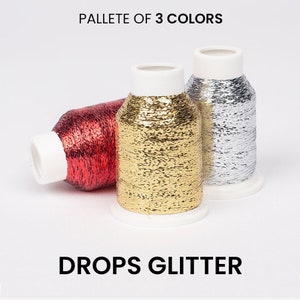 Può includere: Un set di tre bobine di filo con finitura glitterata. I colori sono rosso, oro e argento. Le bobine sono etichettate "Drops Glitter".