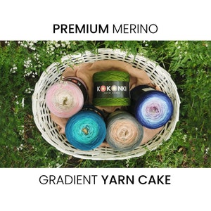 Peut inclure: Cinq gâteaux de laine dégradés dans un panier en osier blanc. Les gâteaux de laine sont dans des tons de rose, vert, bleu, turquoise et beige. La laine est étiquetée "KOKONKI MOTKI OMBRE" et "PREMIUM MERINO GRADIENT YARN CAKE".