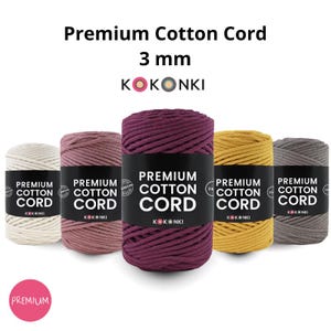 Peut inclure: Cinq bobines de fil de coton Premium, 3 mm d'épaisseur, de différentes couleurs : crème, mauve, violet foncé, jaune moutarde et gris. Chaque bobine a une étiquette noire avec du texte blanc. La marque est KOKONKI.