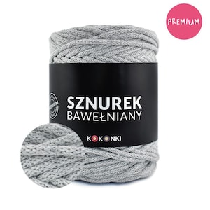Op de afbeelding: Een streng grijs katoenen garen, strak opgerold en gelabeld met de tekst "Sznurek Bawełniany" en het merk "Kokonki". Een roze cirkel met het woord "Premium" staat in de rechterbovenhoek. Een close-up van het garen staat linksonder.