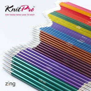 Könnte beinhalten: Ein Set bunter Stricknadeln in verschiedenen Größen von 4,00 mm bis 8,00 mm. Die Nadeln sind fächerförmig angeordnet, wobei die kleinsten Nadeln oben und die größten Nadeln unten liegen. Die Nadeln sind aus Metall und haben eine glänzende Oberfläche. Der Markenname "Knit Pro" ist oben im Bild sichtbar, zusammen mit dem Slogan "Für diejenigen, die es lieben zu stricken". Das Wort "zing" ist unten im Bild sichtbar.
