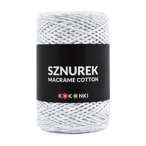 Può includere: Una bobina cilindrica di filo di cotone macramè grigio e bianco. L'etichetta nera mostra la parola "SZNUREK" sopra "MACRAME COTTON" e il marchio "KOKONKI". Il filo è ben avvolto, mostrando una superficie strutturata.