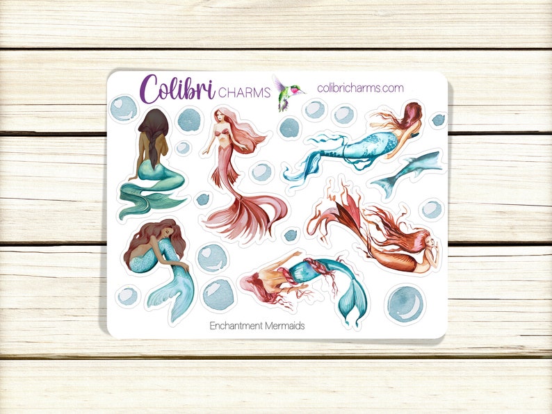 May include: A sheet of stickers featuring watercolor illustrations of mermaids with different colored tails and hair. The stickers are on a white background with the text "Colibri CHARMS" and "colibricharms.com" at the top and "Enchantment Mermaids" at the bottom.