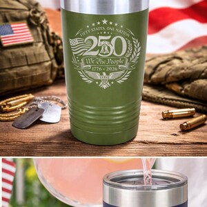 K&ouml;nnte beinhalten: Eine Reihe schwarzer Flachm&auml;nner und isolierter Becher mit patriotischen Designs. Die Flachm&auml;nner und Becher zeigen den Text "250" und "We The People" mit den Jahren 1776-2026, zur Feier des 250. Jahrestages der Vereinigten Staaten.