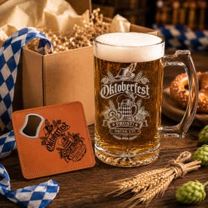 May include: A clear glass beer mug filled with golden beer and foam, featuring an etched Oktoberfest design with the text 'Oktoberfest', 'PROST!', and 'DRINK UP! 2026'. Beside it is a tan leather coaster with a built-in metal bottle opener.