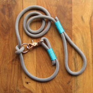 May include: A grey rope dog lead with a matching collar and turquoise accents. The lead has a metal clasp.