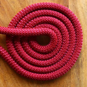 May include: A close-up of a red braided rope coiled into a circle on a wooden surface.