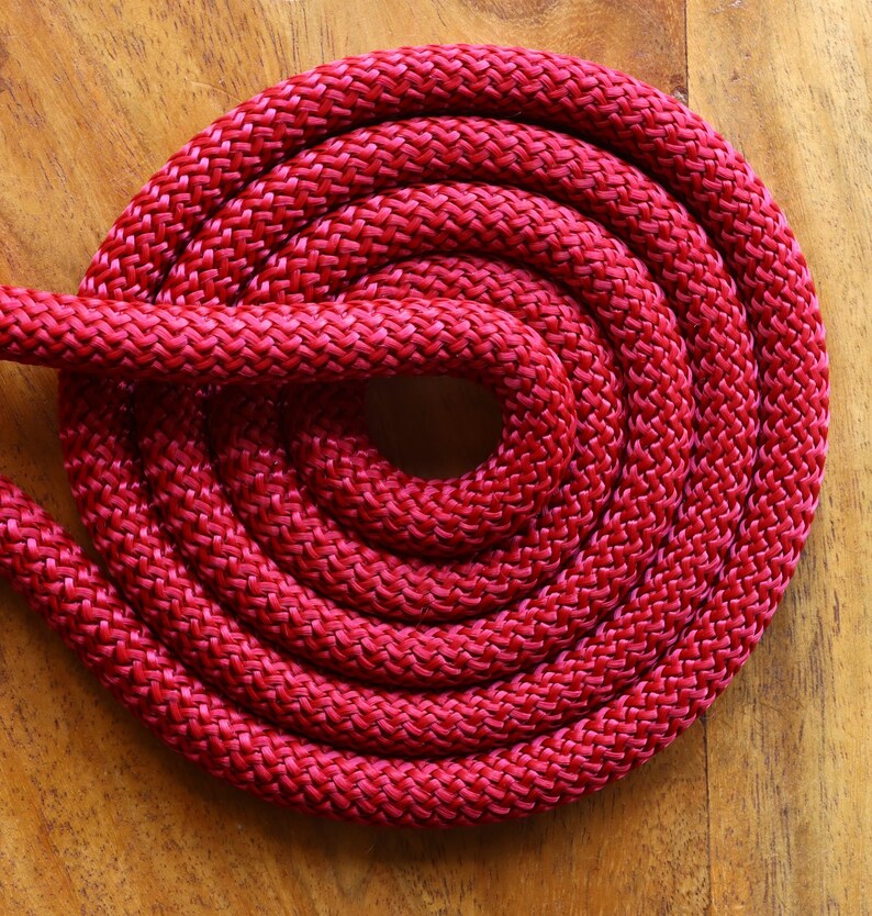 May include: A close-up of a red braided rope coiled into a circle on a wooden surface.