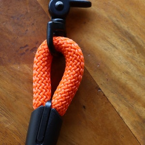 May include: An orange dog leash with a black metal clasp and a black plastic handle. The leash is made of a thick, woven rope material. The clasp is a swivel type, and the handle is a solid piece.