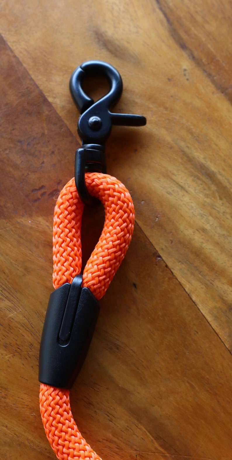 May include: An orange dog leash with a black metal clasp and a black plastic handle. The leash is made of a thick, woven rope material. The clasp is a swivel type, and the handle is a solid piece.