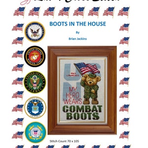 May include: A framed cross-stitch piece with a teddy bear in a military uniform holding an American flag. The text reads "MY HERO WEARS COMBAT BOOTS." The design is surrounded by American flags and military branch emblems. The text "BOOTS IN THE HOUSE" is at the top.