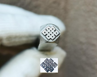 May include: A metal stamping tool featuring a square-shaped head with an engraved eternal knot symbol. The tool is made of polished steel and displays a clear, intricate geometric pattern on its face, designed for creating impressions on surfaces.