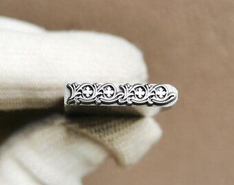 May include: A silver-toned metal stamping tool featuring a rectangular head with an engraved repeating pattern of four-petaled floral motifs connected by scrolling vine-like lines, designed for creating decorative impressions on various surfaces.