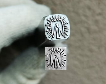 May include: A silver-colored metal stamping tool with a square-shaped head featuring an engraved design of a stylized bird with wings spread, surrounded by a sunburst pattern of short lines. The tool is shown with its stamped impression below.