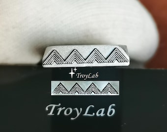 May include: A silver-toned metal stamping tool featuring a repeating geometric pattern of four nested chevron triangles. The tool is engraved with the text TroyLab and includes a small star icon above the brand name on the metal surface.