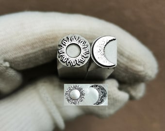 May include: Two silver metal stamping tools featuring a sun and a crescent moon design. The top of each tool displays the engraved motif, while a sample impression of the sun and moon is visible below. The text TroyLab is printed above the tools.