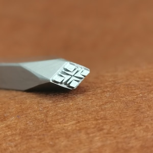 Könnte beinhalten: Nahaufnahme eines silbernen Stempels aus Metall mit einem sternförmigen Design. Der Stempel befindet sich auf einer braunen Oberfläche.