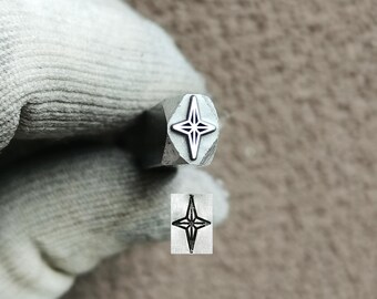 May include: A metal stamping tool featuring a four-pointed star design on its face. The tool is held in a gloved hand, and a sample impression of the star design is shown below the tool. The text TroyLab is visible at the top of the image.