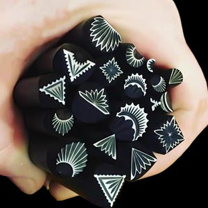 Może przedstawiać: Zbiór czarno-białych stempli metalowych z różnymi wzorami geometrycznymi i kwiatowymi. Stempelki są trzymane w dłoni.