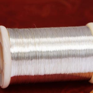 Może przedstawiać: Szpula srebrnego drutu owinięta wok&oacute;ł białej plastikowej szpulki.