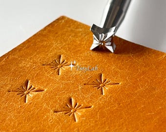 May include: A silver metal stamping tool with a star-shaped tip positioned above a tan leather square. The leather features three impressed star patterns, and the text TroyLab is visible in the center of the leather surface.