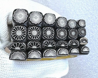 May include: A set of 18 metal stamps featuring a daisy flower design. The stamps are arranged in rows, with the top row featuring a full daisy design and the bottom row featuring a half daisy design.