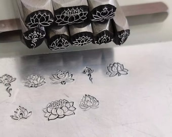 Può includere: Un set di timbri in metallo con disegni di fiori di loto. I timbri sono disposti in fila, con i disegni rivolti verso l'alto. I timbri vengono utilizzati per creare impressioni su metallo o altri materiali.