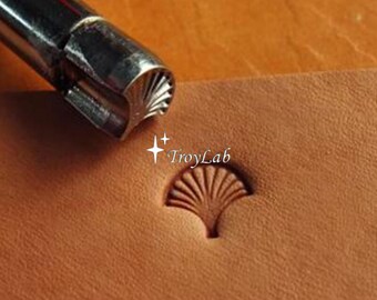 May include: A silver metal leather stamping tool with a fan-shaped tip positioned above a matching impression on a piece of tan leather. The impression features a radial fan pattern. The text TroyLab is printed in white near the center.
